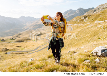 A young woman captures a moment while hiking in a mountainous landscape during golden hour A young woman captures a moment while hiking in a mountainous landscape during golden hour 142408964