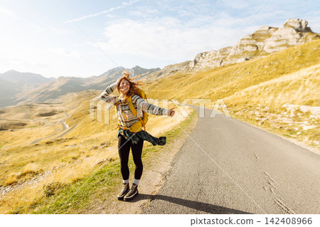 Woman with backpack walking along road with outstretched hand catching car with mountain landscape. Woman with backpack walking along road with outstretched hand catching car with mountain landscape. 142408966