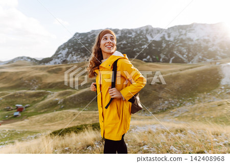 Traveler woman in yellow jacket enjoys hiking on sun. Hiking in mountains with backpacks. Adventure. Traveler woman in yellow jacket enjoys hiking on sun. Hiking in mountains with backpacks. Adventure. 142408968