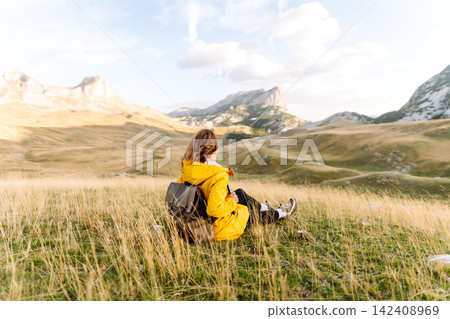 Traveler woman in yellow jacket enjoys hiking on sun. Hiking in mountains with backpacks. Adventure. Traveler woman in yellow jacket enjoys hiking on sun. Hiking in mountains with backpacks. Adventure. 142408969