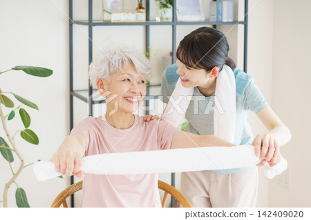 一位日本老婦人和一位年輕的日本護理員正在用毛巾做運動。 一位日本老婦人和一位年輕的日本護理員正在用毛巾做運動。 142409020