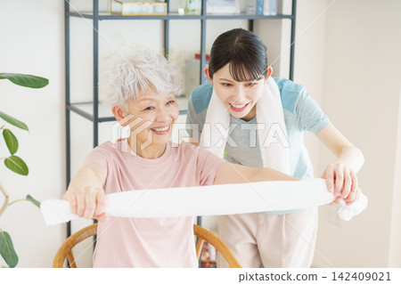 一位日本老婦人和一位年輕的日本護理員正在用毛巾做運動。 一位日本老婦人和一位年輕的日本護理員正在用毛巾做運動。 142409021