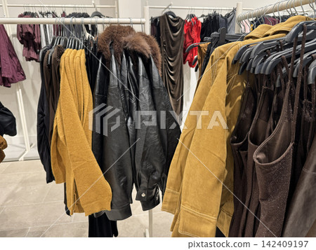 Fashionable Autumn Clothing Collection Hanging On Racks Inside Modern Store Fashionable Autumn Clothing Collection Hanging On Racks Inside Modern Store 142409197