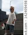 Confident young boy with a cool mohawk hairstyle wears sunglasses and casual streetwear while carrying a sports bag down modern concrete steps in an urban outdoor setting during the day. 142409498