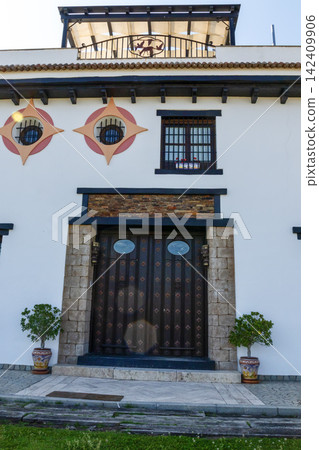 Front view of a white modern house facade with wooden door, stone frame and ceramic pots in El Rocio, Huelva, Spain. Traditional architectural style. Front view of a white modern house facade with wooden door, stone frame and ceramic pots in El Rocio, Huelva, Spain. Traditional architectural style. 142409906
