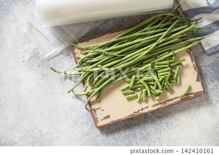 Vacuum sealed fresh green beans in packaging and vacuum sealer on a light grey background, healthy eating, zero waste, meal prep concept. Copy space. Top view flat lay background. Vacuum sealed fresh green beans in packaging and vacuum sealer on a light grey background, healthy eating, zero waste, meal prep concept. Copy space. Top view flat lay background. 142410161