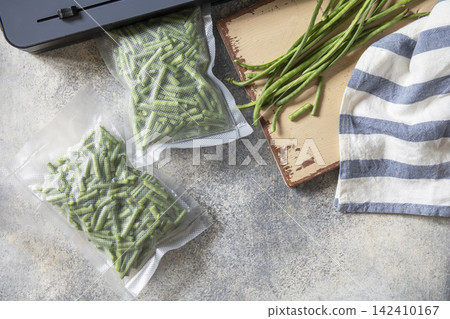 Vacuum sealed fresh green beans in packaging and vacuum sealer on a light grey background, healthy eating, zero waste, meal prep concept. Copy space. Top view flat lay background. Vacuum sealed fresh green beans in packaging and vacuum sealer on a light grey background, healthy eating, zero waste, meal prep concept. Copy space. Top view flat lay background. 142410167