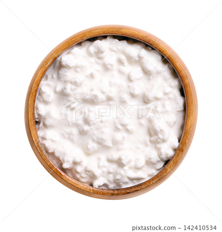 Cottage cheese, type of fresh cheese in wooden bowl, isolated from above. Fresh cheese made from skimmed milk, hence the low milkfat content, with mild flavor and creamy, heterogeneous texture. Photo Cottage cheese, type of fresh cheese in wooden bowl, isolated from above. Fresh cheese made from skimmed milk, hence the low milkfat content, with mild flavor and creamy, heterogeneous texture. Photo 142410534