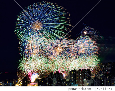 Spectacular colorful fireworks illuminating the night sky above a dense city skyline during a festive celebration. Spectacular colorful fireworks illuminating the night sky above a dense city skyline during a festive celebration. 142411264