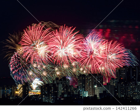 Spectacular colorful fireworks illuminating the night sky above a dense city skyline during a festive celebration. Spectacular colorful fireworks illuminating the night sky above a dense city skyline during a festive celebration. 142411266