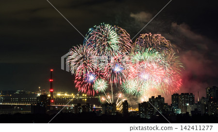 Spectacular colorful fireworks illuminating the night sky above a dense city skyline during a festive celebration. Spectacular colorful fireworks illuminating the night sky above a dense city skyline during a festive celebration. 142411277