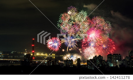 Spectacular colorful fireworks illuminating the night sky above a dense city skyline during a festive celebration. Spectacular colorful fireworks illuminating the night sky above a dense city skyline during a festive celebration. 142411278
