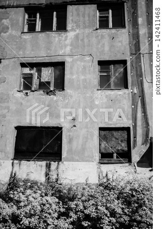 Decaying facade of an abandoned Soviet-era residential building in Kukisvumchorr, Kirovsk, Murmansk Region, Russia. Exposed red brickwork, crumbling plaster, broken windows and boarded openings show t 142411468