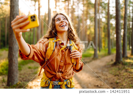Selfie time! Young woman enjoying a sunny hike in a lush forest with a backpack on a warm day Selfie time! Young woman enjoying a sunny hike in a lush forest with a backpack on a warm day 142411951