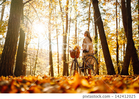 Stylish woman with a bicycle enjoying autumn weather in the park. Beautiful Woman in the autumn forest. Stylish woman with a bicycle enjoying autumn weather in the park. Beautiful Woman in the autumn forest. 142412025