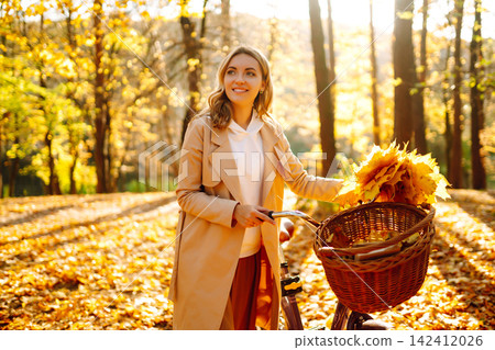 Stylish woman with a bicycle enjoying autumn weather in the park. Beautiful Woman in the autumn forest. Stylish woman with a bicycle enjoying autumn weather in the park. Beautiful Woman in the autumn forest. 142412026