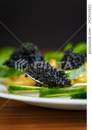 Black caviar and cucumber served on pancake on wooden background Black caviar and cucumber served on pancake on wooden background 142412421