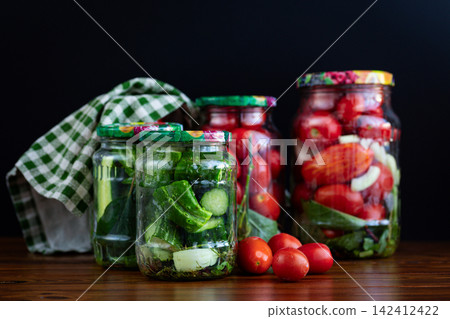 Homemade pickled tomatoes in glass jars on dark background Homemade pickled tomatoes in glass jars on dark background 142412422