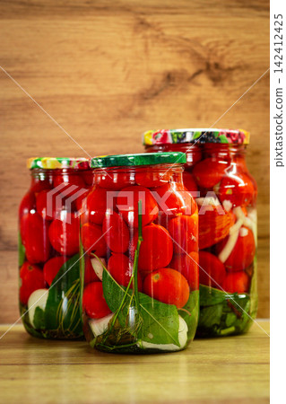 Preserved red tomatoes with herbs in jars on wooden background Preserved red tomatoes with herbs in jars on wooden background 142412425