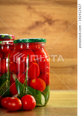 Red preserved tomatoes in sealed jars against wooden background Red preserved tomatoes in sealed jars against wooden background 142412427