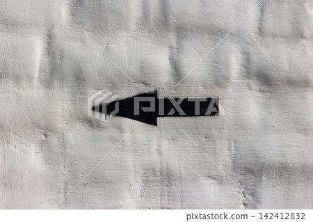 Black spray-painted arrow icon pointing left on a rugged white plastered wall, minimalist urban street art style with a gritty texture and sharp contrast, creative simple navigational symbol Black spray-painted arrow icon pointing left on a rugged white plastered wall, minimalist urban street art style with a gritty texture and sharp contrast, creative simple navigational symbol 142412832