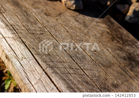 Weathered wooden board with deep rustic grain and textured cracks, bathed in warm natural sunlight creating a high contrast surface, perfect for a vintage organic rustic background design Weathered wooden board with deep rustic grain and textured cracks, bathed in warm natural sunlight creating a high contrast surface, perfect for a vintage organic rustic background design 142412853