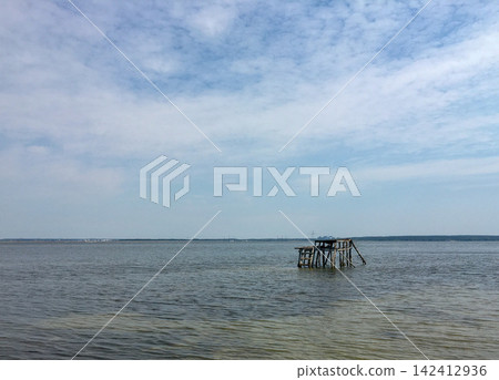 Old wooden pier structure in calm water under cloudy sky Old wooden pier structure in calm water under cloudy sky 142412936