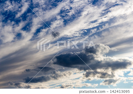 Dramatic sky with feathery cirrus clouds drifting across deep blue expanse, sunlight catching edges of fluffy cumulus formations creates a stunning natural masterpiece for atmospheric backgrounds Dramatic sky with feathery cirrus clouds drifting across deep blue expanse, sunlight catching edges of fluffy cumulus formations creates a stunning natural masterpiece for atmospheric backgrounds 142413095
