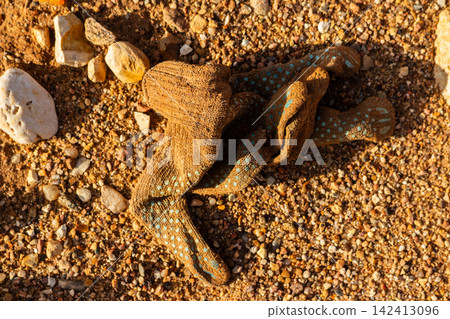 Dirty brown knitted work glove with blue anti-slip dots abandoned on dry rocky ground, discarded construction gear left on textured desert gravel surface during golden hour sunlight Dirty brown knitted work glove with blue anti-slip dots abandoned on dry rocky ground, discarded construction gear left on textured desert gravel surface during golden hour sunlight 142413096