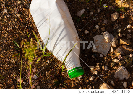 Discarded white plastic bottle with green cap lying on dry stony ground, representing environmental pollution and human impact on nature, high angle view of abandoned trash outdoor Discarded white plastic bottle with green cap lying on dry stony ground, representing environmental pollution and human impact on nature, high angle view of abandoned trash outdoor 142413100