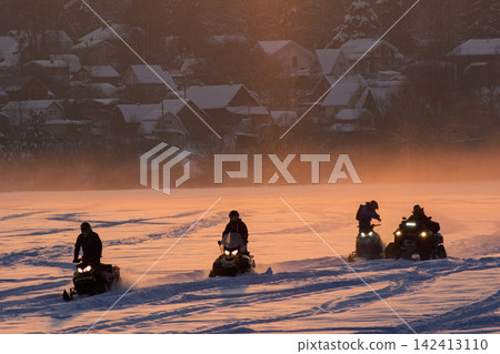 Powerful snowmobiles speed across a vast, sun-drenched snowy field, leaving fresh tracks in the glistening powder during a vibrant, golden hour winter landscape journey Powerful snowmobiles speed across a vast, sun-drenched snowy field, leaving fresh tracks in the glistening powder during a vibrant, golden hour winter landscape journey 142413110