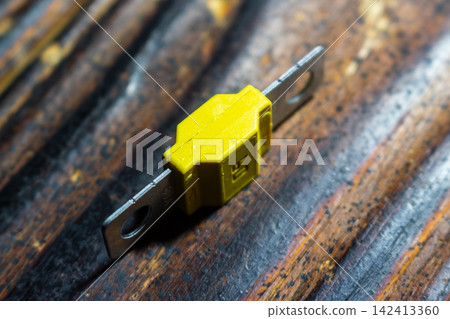 Yellow 60A Midival automotive fuse with metal terminals placed on a dark wooden textured surface for electrical system protection and circuit safety maintenance closeup shot Yellow 60A Midival automotive fuse with metal terminals placed on a dark wooden textured surface for electrical system protection and circuit safety maintenance closeup shot 142413360