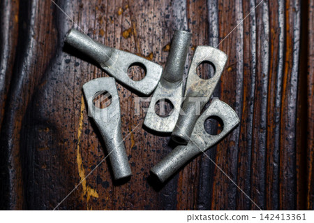 A collection of tinned copper cable lugs scattered on a dark textured wooden surface, essential electrical hardware components for secure and reliable wiring connections in industrial projects A collection of tinned copper cable lugs scattered on a dark textured wooden surface, essential electrical hardware components for secure and reliable wiring connections in industrial projects 142413361