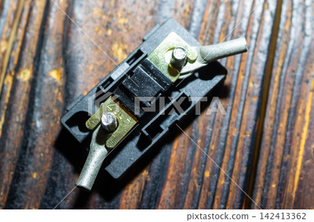 Close-up of a 200A miniANL fuse mounted in a black plastic holder with the protective cover removed, showing metal terminals on a rustic wooden background 142413362