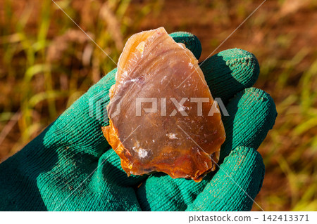 A close-up shot of a freshly broken brown flint stone held in hand, showing characteristic conchoidal fracture waves and sharp edges used in prehistoric tools A close-up shot of a freshly broken brown flint stone held in hand, showing characteristic conchoidal fracture waves and sharp edges used in prehistoric tools 142413371