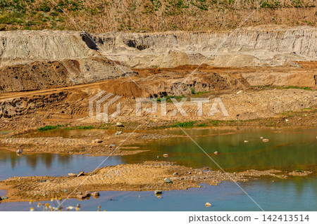 Industrial sand quarry landscape featuring textured brown soil, deep excavation layers, and muddy water pools under bright summer daylight, showcasing raw earth and terrain extraction site Industrial sand quarry landscape featuring textured brown soil, deep excavation layers, and muddy water pools under bright summer daylight, showcasing raw earth and terrain extraction site 142413514