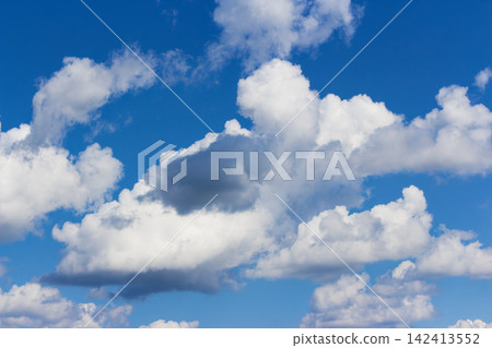 Fluffy white clouds drifting across a vibrant azure sky creating a bright atmosphere with a touch of contrast from a darker storm cloud formation on a sunny day Fluffy white clouds drifting across a vibrant azure sky creating a bright atmosphere with a touch of contrast from a darker storm cloud formation on a sunny day 142413552