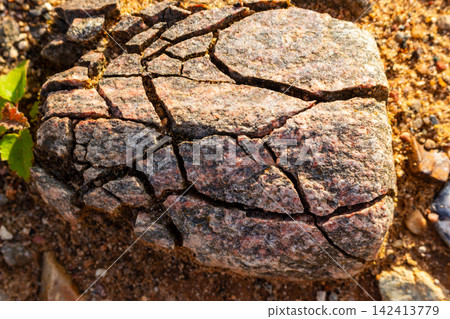 Mechanical weathering of a pink granite boulder under frost action. Concept of collapse, crisis and fragile structure shown by cracked rock 142413779