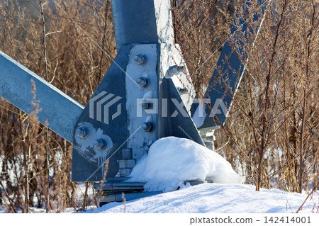 Close-up detail of a galvanized steel electricity pylon base junction bolted and covered with fresh winter snow in a rustic field setting during a sunny cold day Close-up detail of a galvanized steel electricity pylon base junction bolted and covered with fresh winter snow in a rustic field setting during a sunny cold day 142414001