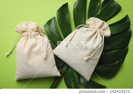 Cotton eco bags and monstera leaf on green background, flat lay 142414073