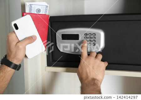 Man opening black steel safe with electronic lock at hotel, closeup Man opening black steel safe with electronic lock at hotel, closeup 142414297