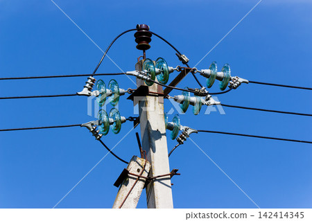 Concrete utility pole with glass insulators holding electrical power lines against a clear blue sky, showing industrial equipment for energy distribution and high voltage grid infrastructure 142414345