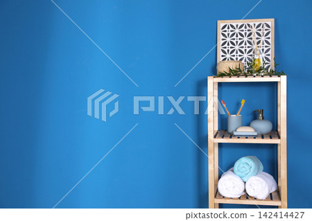 Shelving unit with toiletries near blue wall indoors, space for text. Bathroom interior element Shelving unit with toiletries near blue wall indoors, space for text. Bathroom interior element 142414427