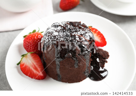 Delicious warm chocolate lava cake with mint and strawberries on table, closeup Delicious warm chocolate lava cake with mint and strawberries on table, closeup 142414533