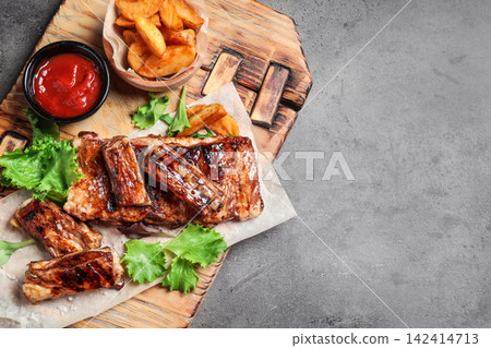 Delicious grilled ribs and garnish on grey table, top view. Space for text Delicious grilled ribs and garnish on grey table, top view. Space for text 142414713