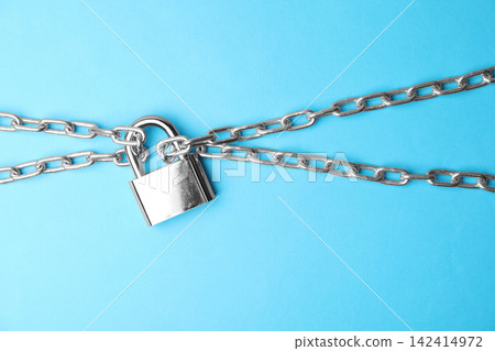Steel padlock and chains on light blue background, top view. Safety concept Steel padlock and chains on light blue background, top view. Safety concept 142414972