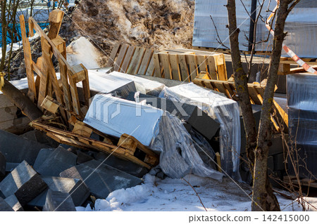 Toppled concrete blocks stacked on wooden pallets, wrapped in plastic film on a construction site amidst melting snow and debris during a cold winter day at the outdoor warehouse Toppled concrete blocks stacked on wooden pallets, wrapped in plastic film on a construction site amidst melting snow and debris during a cold winter day at the outdoor warehouse 142415000