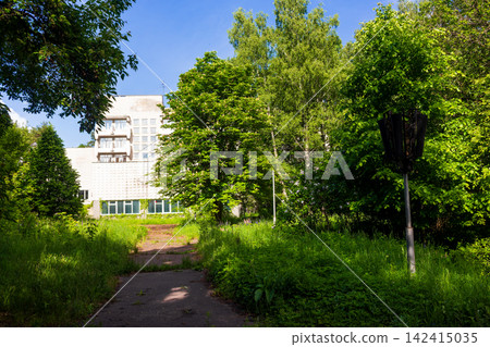 Soviet era sanatorium building nestled within a lush green forest, displaying architectural features of a quiet, dormant resort facility surrounded by dense summer vegetation at daytime Soviet era sanatorium building nestled within a lush green forest, displaying architectural features of a quiet, dormant resort facility surrounded by dense summer vegetation at daytime 142415035