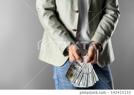 Man in handcuffs holding bribe money on grey background, closeup Man in handcuffs holding bribe money on grey background, closeup 142415133