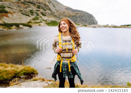 Hiking near a lake in mountain area with a woman wearing a yellow jacket and backpack during daytime Hiking near a lake in mountain area with a woman wearing a yellow jacket and backpack during daytime 142415183